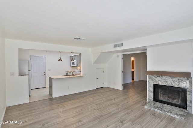 unfurnished living room featuring a premium fireplace and light hardwood / wood-style flooring