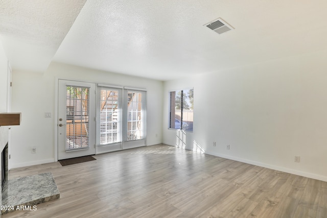 unfurnished living room with a textured ceiling and light hardwood / wood-style floors