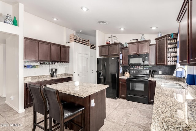 kitchen with sink, a breakfast bar, a center island, light stone counters, and black appliances