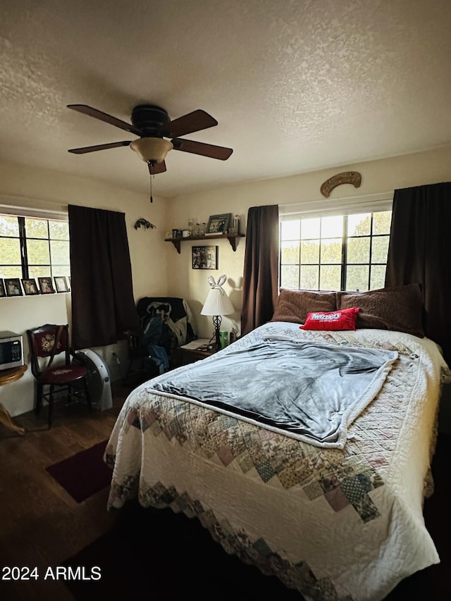 bedroom with ceiling fan, wood-type flooring, and a textured ceiling