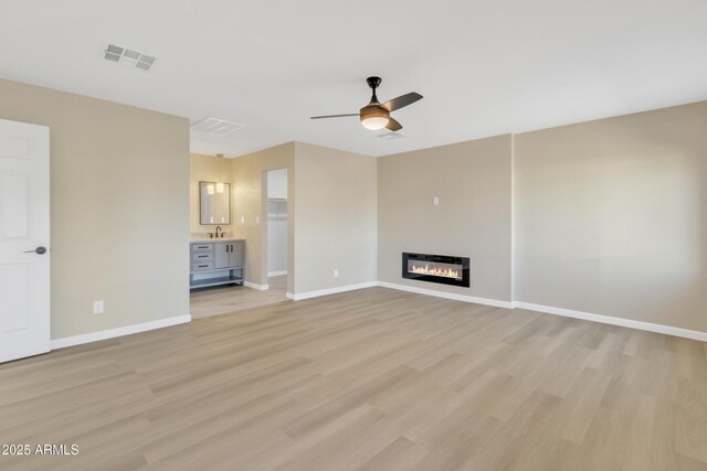 7607 N 42nd Ln, Phoenix, AZ 85051 - unfurnished living room featuring a ceiling fan, light wood-style floors, baseboards, a sink, and a glass covered fireplace