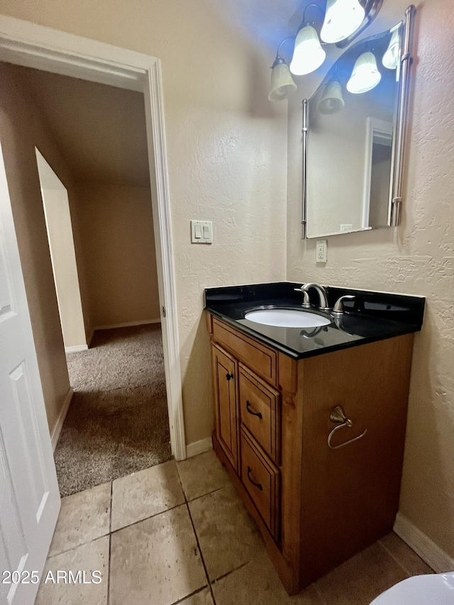 half bathroom featuring a textured wall, tile patterned floors, baseboards, and vanity