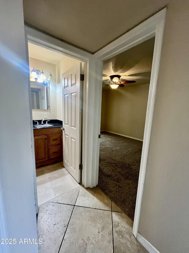 hall with light tile patterned floors, baseboards, a sink, and light colored carpet