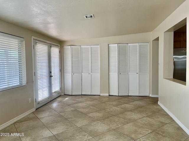 unfurnished bedroom with freestanding refrigerator, visible vents, baseboards, and two closets