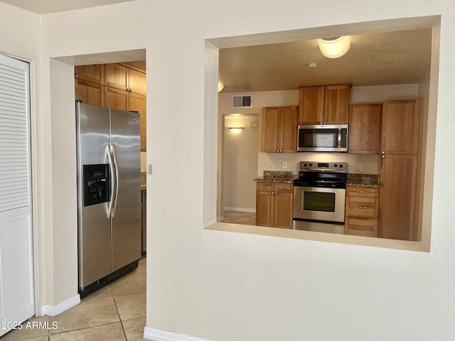 kitchen featuring light tile patterned floors, stainless steel appliances, visible vents, and brown cabinets