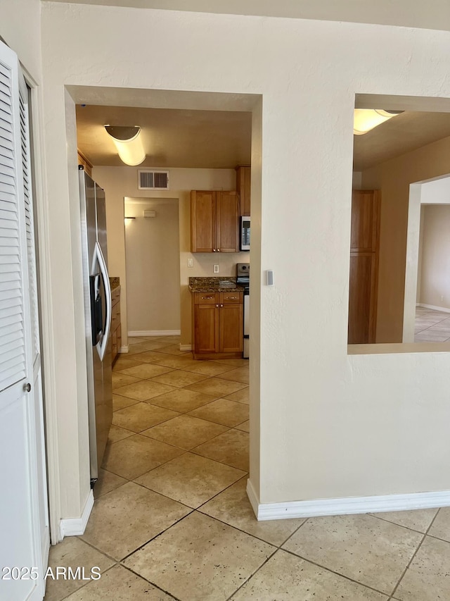 kitchen featuring brown cabinets, visible vents, appliances with stainless steel finishes, light tile patterned flooring, and baseboards