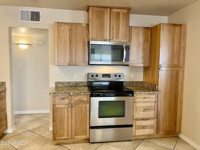 kitchen featuring light tile patterned floors, visible vents, appliances with stainless steel finishes, dark stone counters, and baseboards