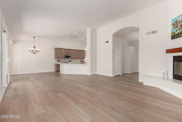 4010 N 156th Ln, Goodyear, AZ 85395 - unfurnished living room with visible vents, a notable chandelier, a large fireplace, light wood-style flooring, and lofted ceiling