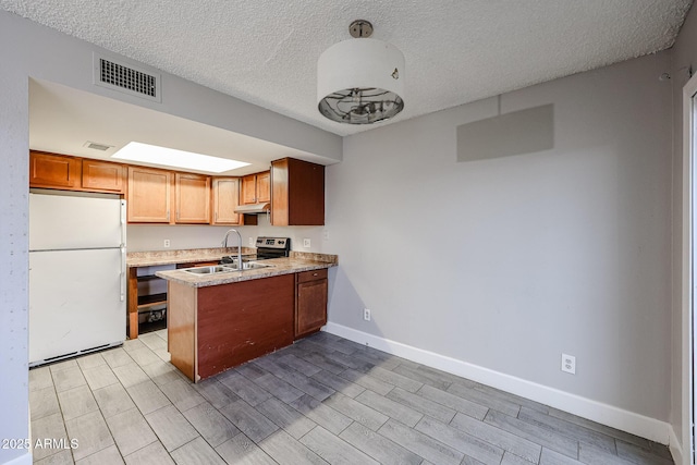 kitchen featuring visible vents, light countertops, a peninsula, freestanding refrigerator, and a sink