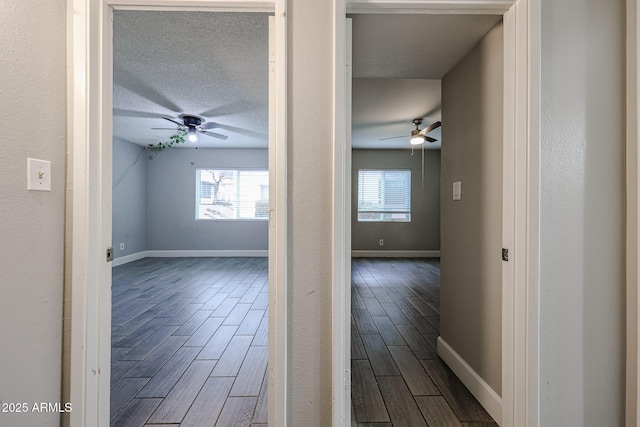 hallway with baseboards, a textured ceiling, and wood finish floors