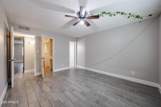 unfurnished bedroom featuring wood finished floors, baseboards, visible vents, a spacious closet, and a textured ceiling