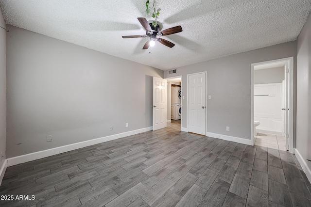 unfurnished bedroom with stacked washer / drying machine, baseboards, a textured ceiling, and dark wood finished floors