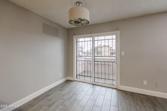 spare room featuring baseboards, a textured ceiling, and wood tiled floor