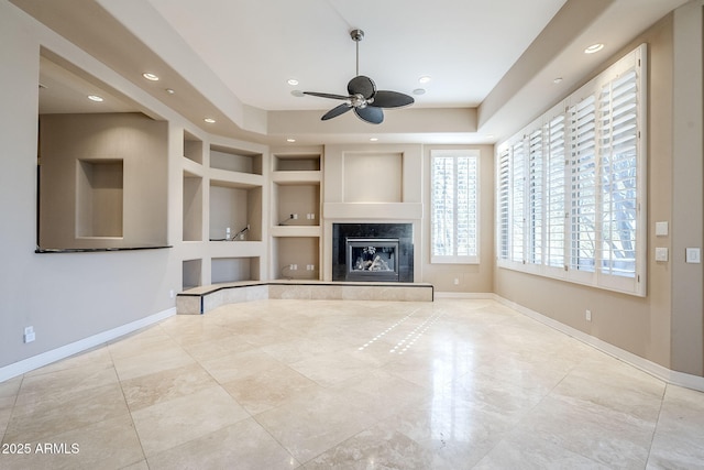 unfurnished living room featuring light tile patterned floors, built in features, a premium fireplace, ceiling fan, and a tray ceiling