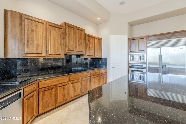 kitchen featuring built in appliances, decorative backsplash, dark stone countertops, and light tile patterned flooring