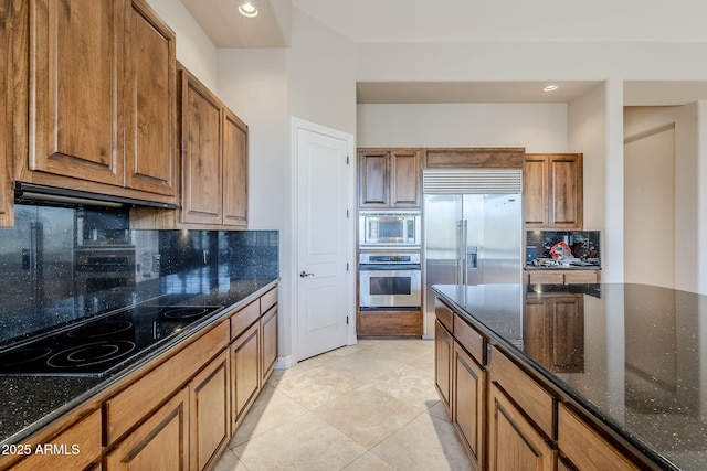 kitchen with tasteful backsplash, built in appliances, ventilation hood, light tile patterned floors, and dark stone countertops