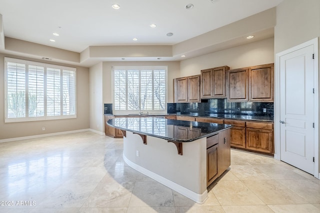 kitchen featuring a kitchen bar, sink, a center island, dark stone countertops, and decorative backsplash