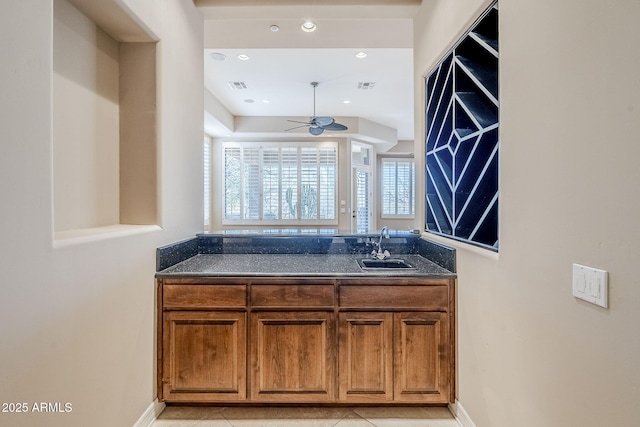 kitchen with sink, dark stone countertops, ceiling fan, and light tile patterned floors