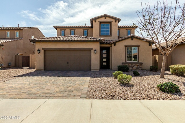 mediterranean / spanish home featuring stucco siding, decorative driveway, fence, a garage, and a tiled roof