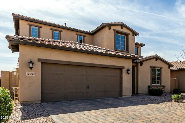 mediterranean / spanish house with stucco siding, a tiled roof, and decorative driveway