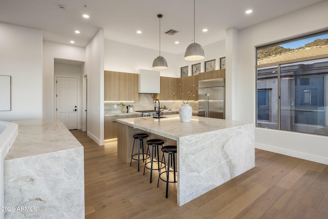 13631 E Windrose Dr, Scottsdale, AZ 85259 - kitchen featuring built in fridge, modern cabinets, wood finished floors, a large island with sink, and light stone countertops
