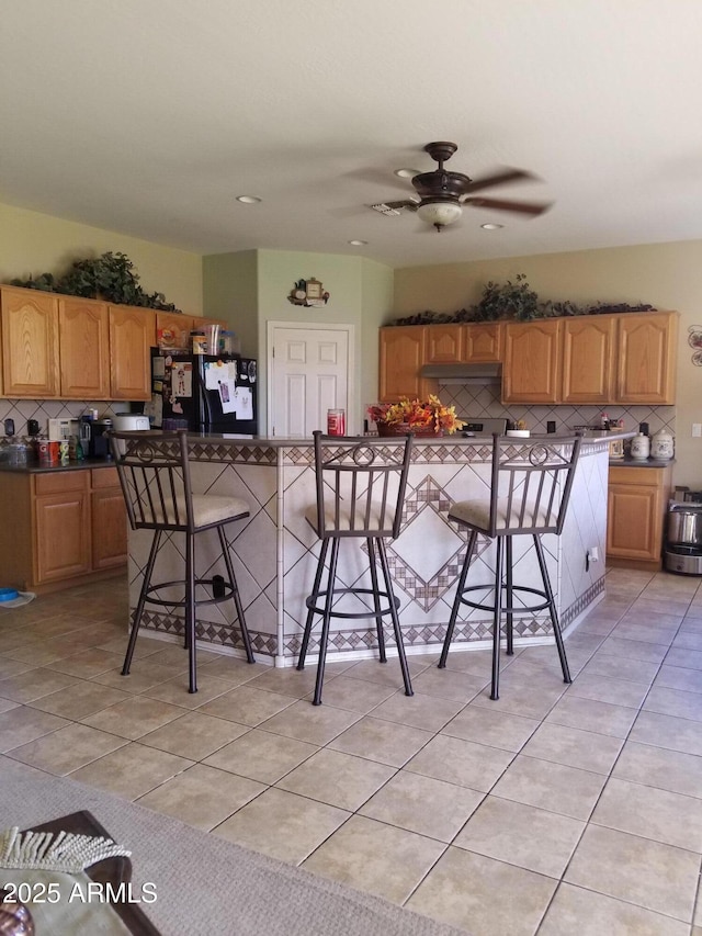 kitchen with black refrigerator, ceiling fan, a kitchen bar, decorative backsplash, and light tile patterned flooring