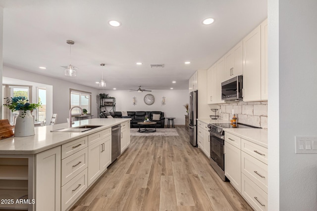 kitchen featuring appliances with stainless steel finishes, decorative light fixtures, white cabinetry, light hardwood / wood-style floors, and sink