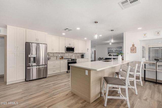 kitchen featuring appliances with stainless steel finishes, white cabinetry, sink, pendant lighting, and a breakfast bar area