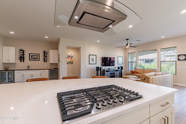 kitchen featuring stainless steel gas stovetop, ceiling fan, light hardwood / wood-style flooring, and beverage cooler