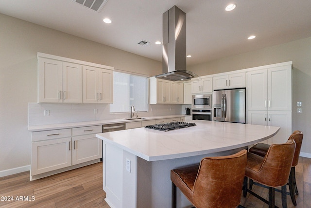 kitchen featuring appliances with stainless steel finishes, sink, island exhaust hood, a center island, and light hardwood / wood-style flooring