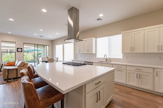 kitchen with stainless steel gas stovetop, island range hood, sink, light hardwood / wood-style floors, and a center island