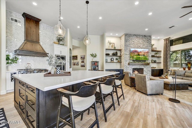 kitchen with a large island, hanging light fixtures, a fireplace, white cabinets, and custom range hood