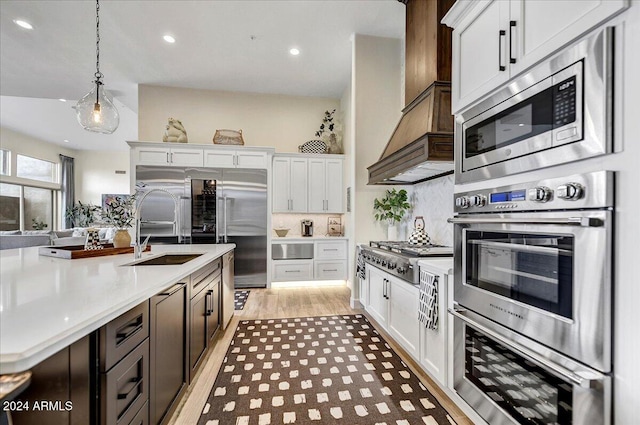 kitchen featuring built in appliances, decorative light fixtures, light hardwood / wood-style floors, and white cabinets