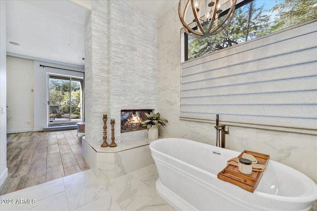 bathroom featuring wood-type flooring, an inviting chandelier, tile walls, a fireplace, and a bathing tub