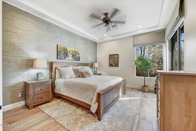 bedroom with ceiling fan, a tray ceiling, and light hardwood / wood-style flooring