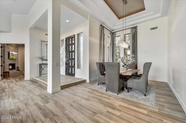 dining area featuring light hardwood / wood-style floors, a raised ceiling, and a brick fireplace