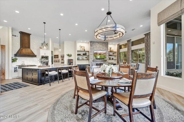 dining area with a large fireplace, a notable chandelier, and light wood-type flooring