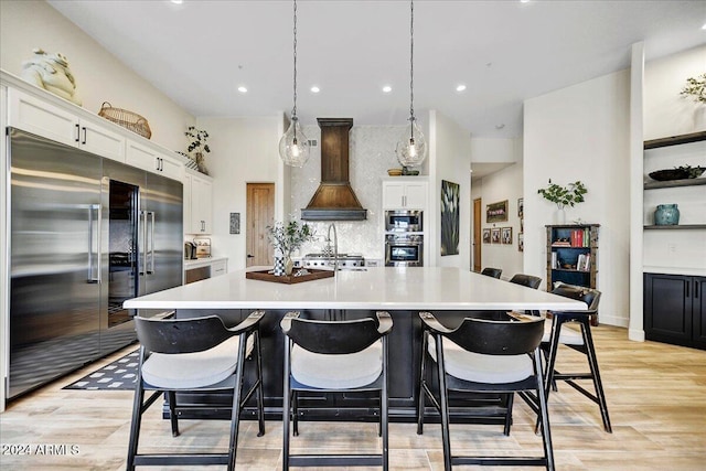 kitchen featuring light wood-type flooring, a spacious island, built in appliances, white cabinetry, and hanging light fixtures