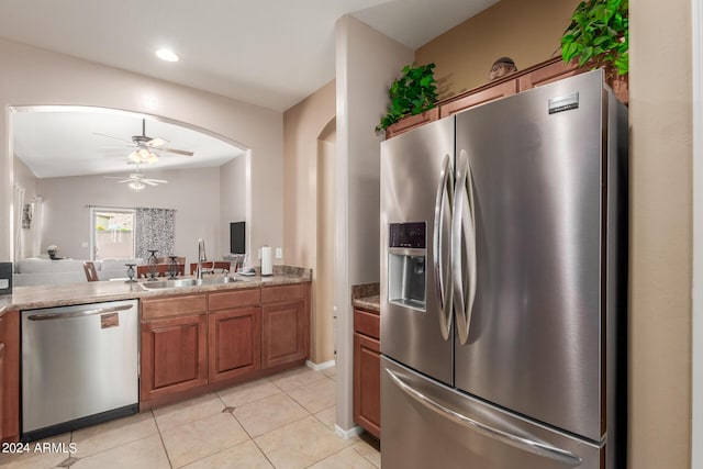 kitchen featuring sink, light tile patterned floors, appliances with stainless steel finishes, stone counters, and ceiling fan