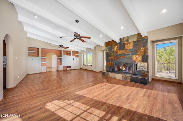 unfurnished living room featuring hardwood / wood-style floors, lofted ceiling with beams, a stone fireplace, and a wealth of natural light