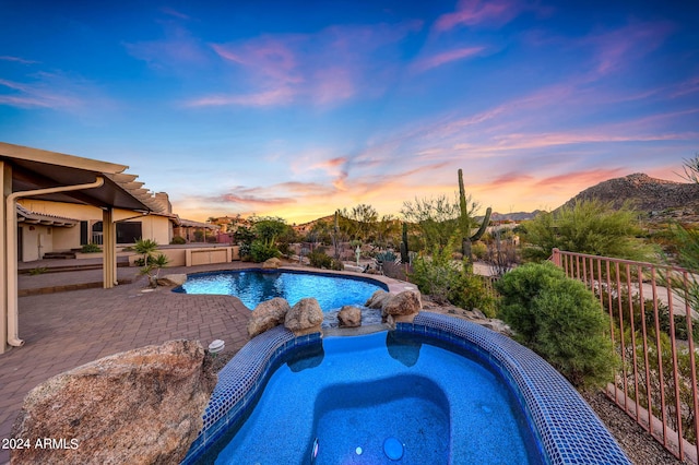 pool at dusk with an in ground hot tub and a patio