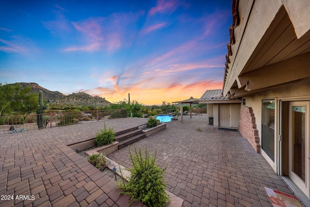 patio terrace at dusk featuring a fenced in pool and a mountain view