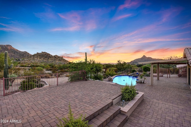 patio terrace at dusk with a mountain view and a fenced in pool