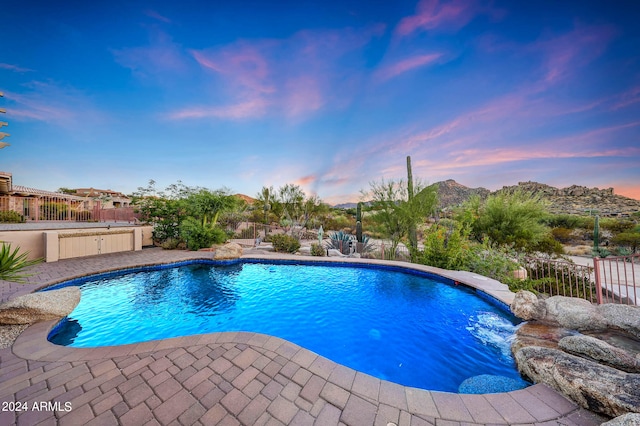 pool at dusk featuring pool water feature and a patio