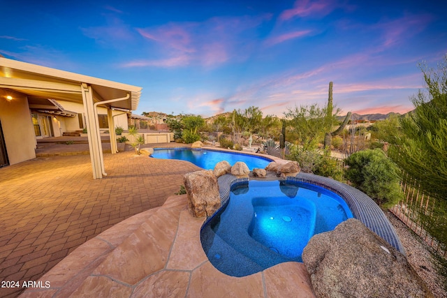 pool at dusk with a patio area and an in ground hot tub