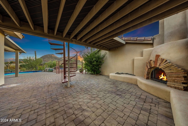 patio terrace at dusk with a mountain view, a fenced in pool, and an outdoor fireplace