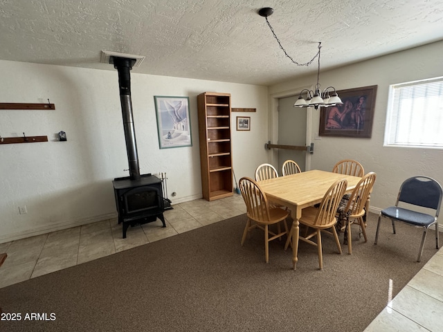 dining space featuring an inviting chandelier, a wood stove, light tile patterned floors, and a textured ceiling