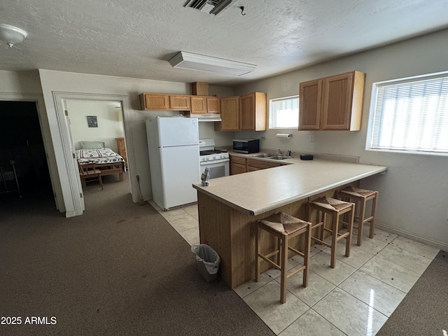 kitchen featuring sink, white appliances, a breakfast bar area, a textured ceiling, and kitchen peninsula