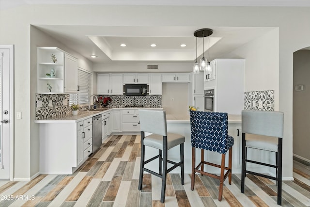 kitchen featuring a breakfast bar area, a tray ceiling, stainless steel appliances, and white cabinetry