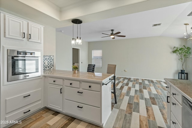 kitchen with hanging light fixtures, white cabinets, oven, and light wood-type flooring